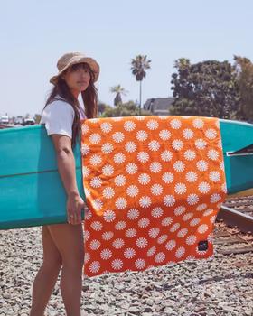A woman holding a surfboard with an orange slowtide towel draped over it
