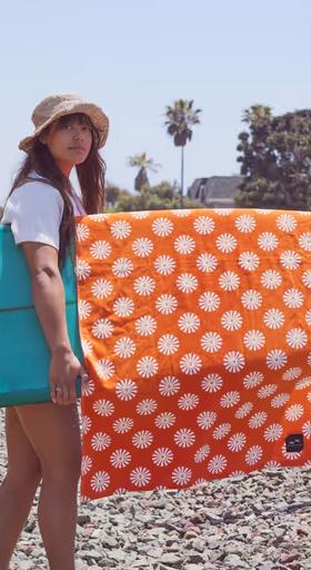 A woman holding a surfboard with an orange slowtide towel draped over it
