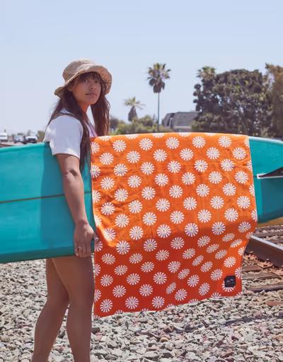 A woman holding a surfboard with an orange slowtide towel draped over it