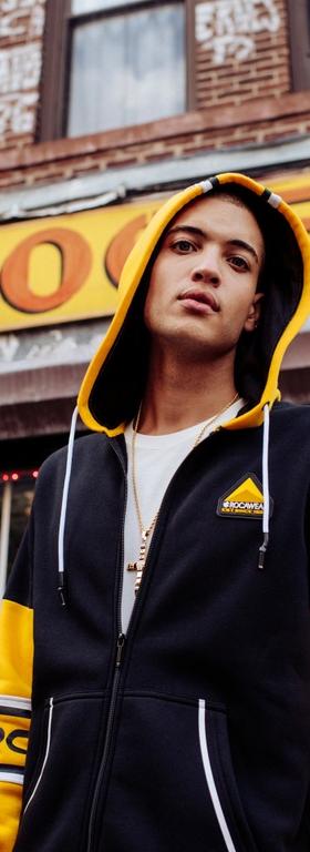 A man wearing a Rocawear yellow and black zip-up hoodie