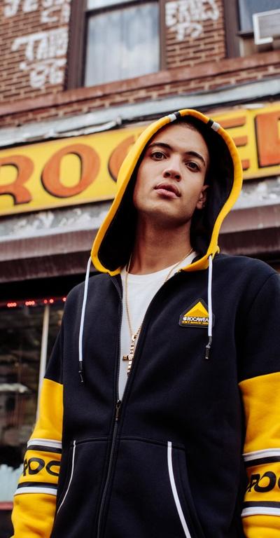 A man wearing a Rocawear yellow and black zip-up hoodie