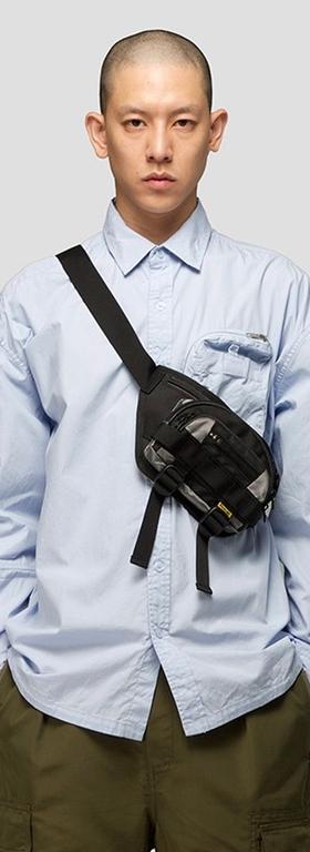 A man wearing a 4DIMENSION outfit featuring a light blue button up and a black bag slinged across chest