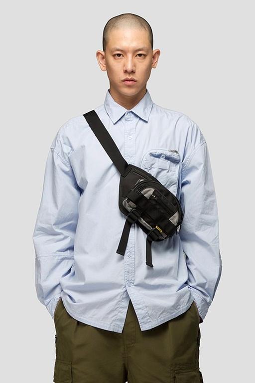 A man wearing a 4DIMENSION outfit featuring a light blue button up and a black bag slinged across chest
