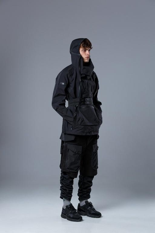 A man wearing a RIOT DIVISION black outfit featuring a technical jacket and pants