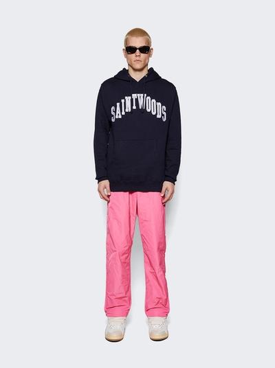 A man wearing a saintwoods branded navy hoodie with pink pants and sunglasses