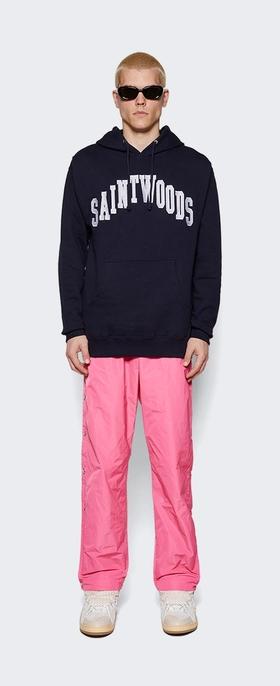 A man wearing a saintwoods branded navy hoodie with pink pants and sunglasses