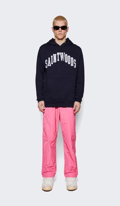 A man wearing a saintwoods branded navy hoodie with pink pants and sunglasses