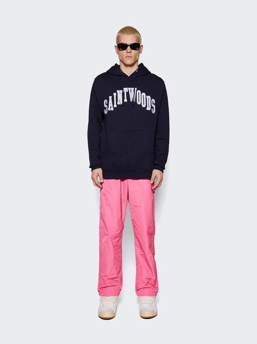 A man wearing a saintwoods branded navy hoodie with pink pants and sunglasses