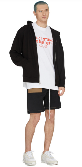 A man wearing a Malice Studios branded t-shirt with a sweater and shorts