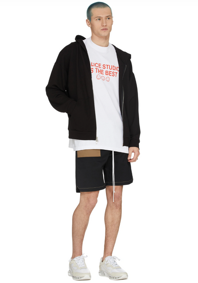 A man wearing a Malice Studios branded t-shirt with a sweater and shorts