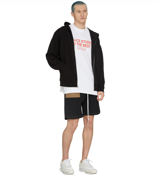 A man wearing a Malice Studios branded t-shirt with a sweater and shorts