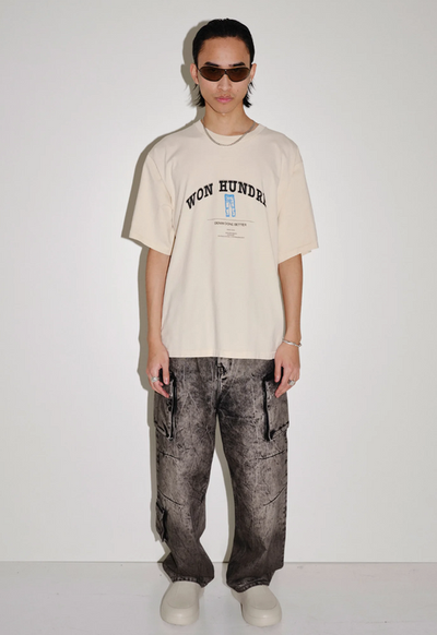 A man wearing a won hundred beige branded t-shirt and oversize black jeans