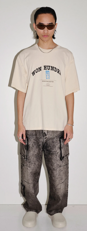 A man wearing a won hundred beige branded t-shirt and oversize black jeans