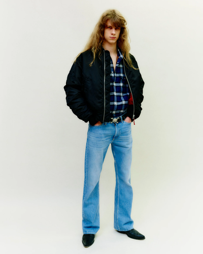 A man wearing a retro Stockholm Surfboard Club jacket, plaid and bell-bottomed jeans