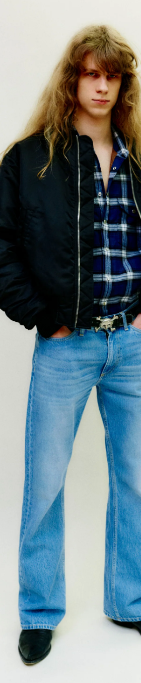 A man wearing a retro Stockholm Surfboard Club jacket, plaid and bell-bottomed jeans