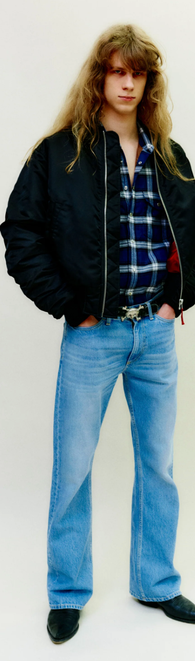 A man wearing a retro Stockholm Surfboard Club jacket, plaid and bell-bottomed jeans
