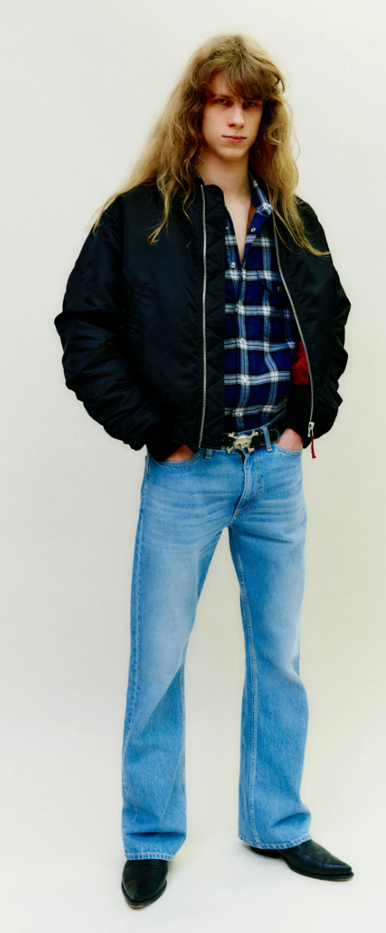 A man wearing a retro Stockholm Surfboard Club jacket, plaid and bell-bottomed jeans