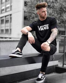 A man wearing a black vans t-shirt with black vans shoes with the classic white stripe