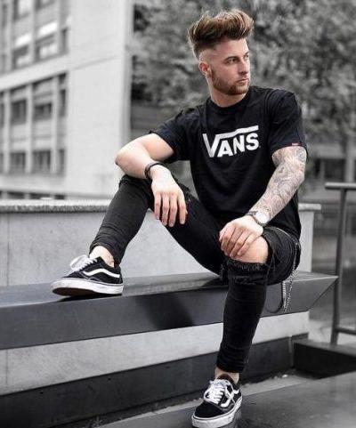 A man wearing a black vans t-shirt with black vans shoes with the classic white stripe