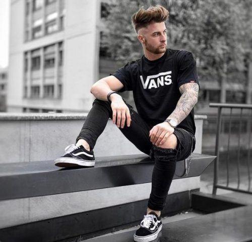 A man wearing a black vans t-shirt with black vans shoes with the classic white stripe