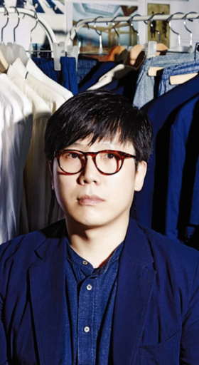 A man wearing a Document blue button up and cardigan surrounded by button up shirts