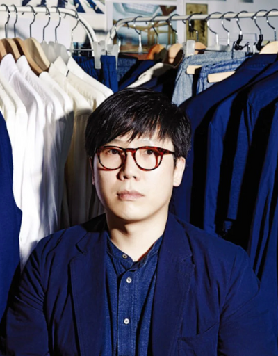 A man wearing a Document blue button up and cardigan surrounded by button up shirts