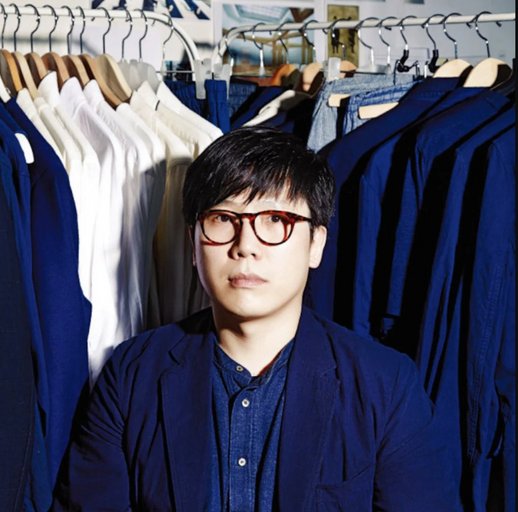 A man wearing a Document blue button up and cardigan surrounded by button up shirts