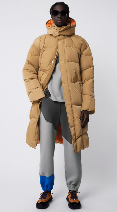 A man wearing a puffy beige Ader-error jacket with grey pants