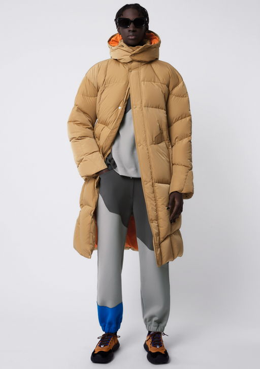 A man wearing a puffy beige Ader-error jacket with grey pants
