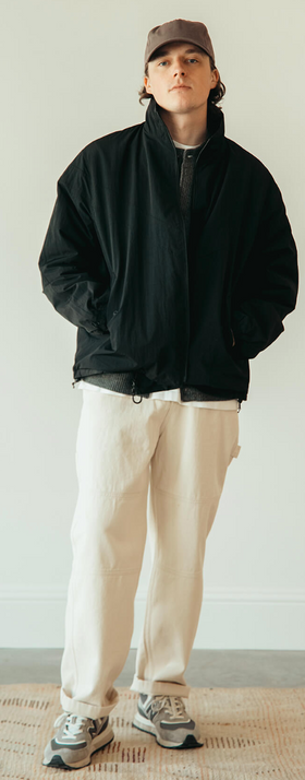 A man wearing a black frizmworks jacket and beige pants