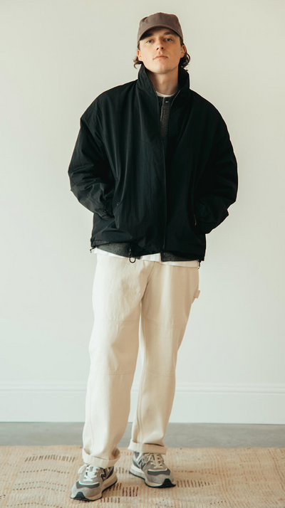 A man wearing a black frizmworks jacket and beige pants
