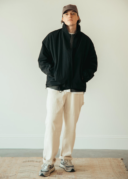 A man wearing a black frizmworks jacket and beige pants