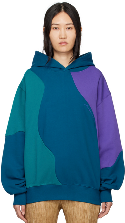 A woman wearing a colorful blue, purple and green Andersson Bell hoodie