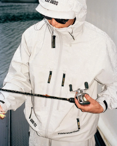 A man wearing a white technical jacket with hood on by thisisneverthat