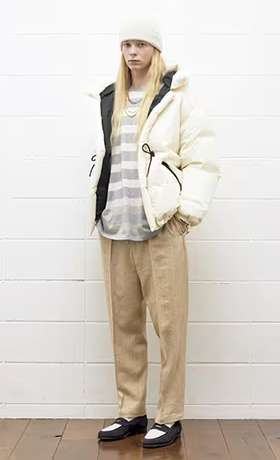 A woman wearing a cream puffy UNUSED Japan with striped grey and white sweater and brown pants