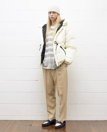 A woman wearing a cream puffy UNUSED Japan with striped grey and white sweater and brown pants