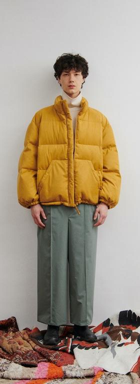 A man wearing a clean orange DIGAWEL puffy jacket with oversize slacks