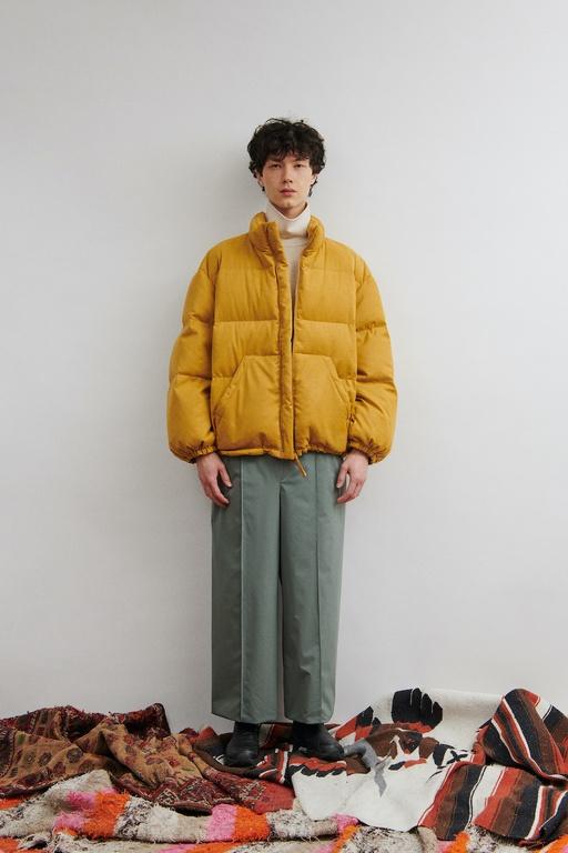 A man wearing a clean orange DIGAWEL puffy jacket with oversize slacks