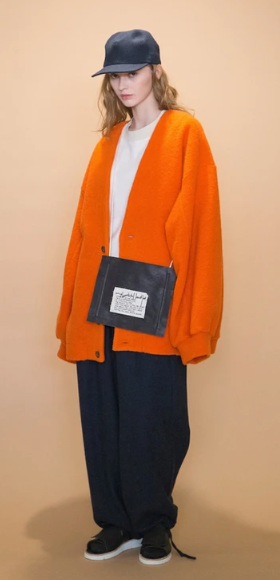 A woman wearing an oversized orange my beautiful landlet cardigan and white t-shirt