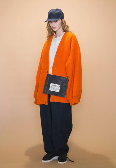 A woman wearing an oversized orange my beautiful landlet cardigan and white t-shirt