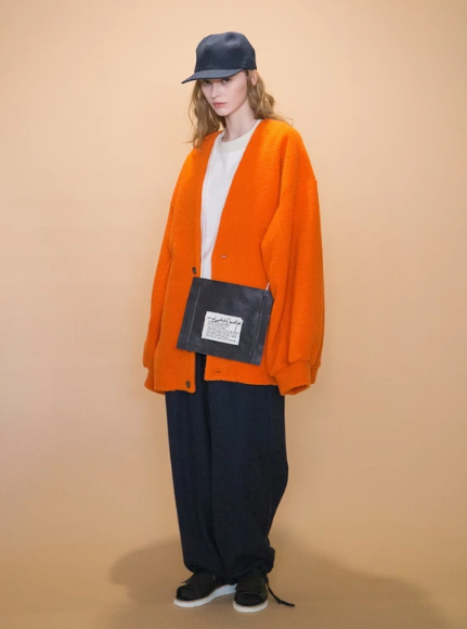 A woman wearing an oversized orange my beautiful landlet cardigan and white t-shirt