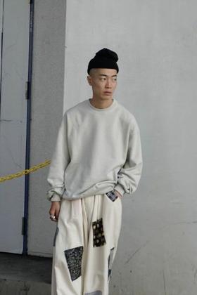 A man wearing a 1LDK grey sweater, black beanie and patched baggy pants