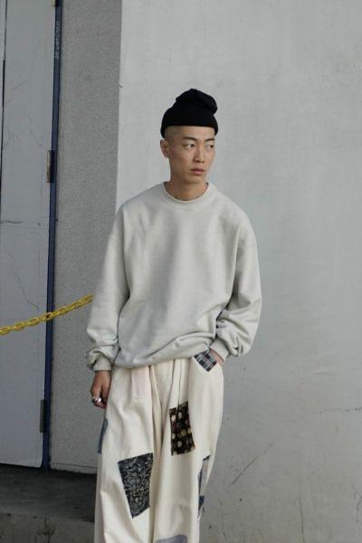 A man wearing a 1LDK grey sweater, black beanie and patched baggy pants