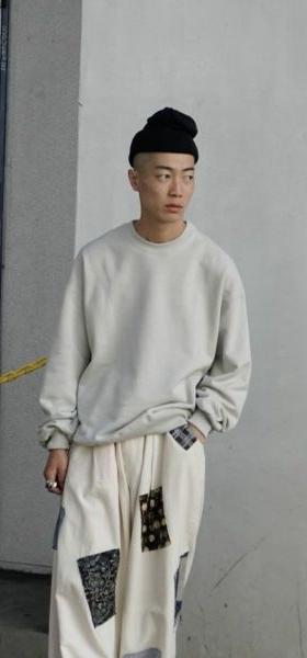 A man wearing a 1LDK grey sweater, black beanie and patched baggy pants