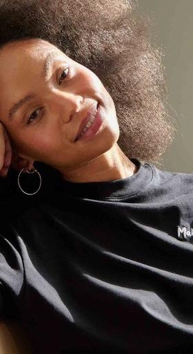 A woman wearing a black Maha logo t-shirt