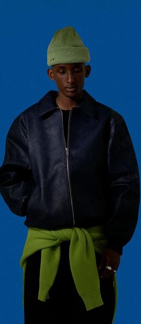 A man wearing a dark Arte Antwerp jacket with a green beanie and matching green sweater