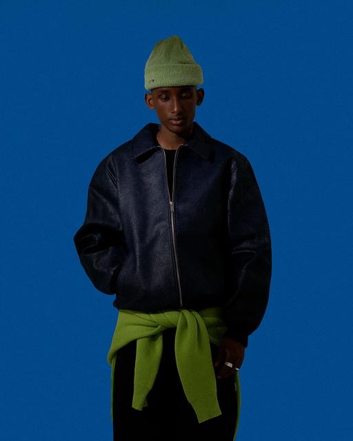 A man wearing a dark Arte Antwerp jacket with a green beanie and matching green sweater