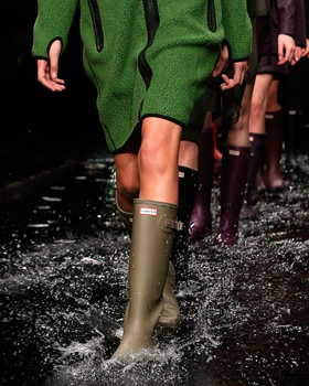 A woman walking the runway wearing a pair of green Hunter Boots