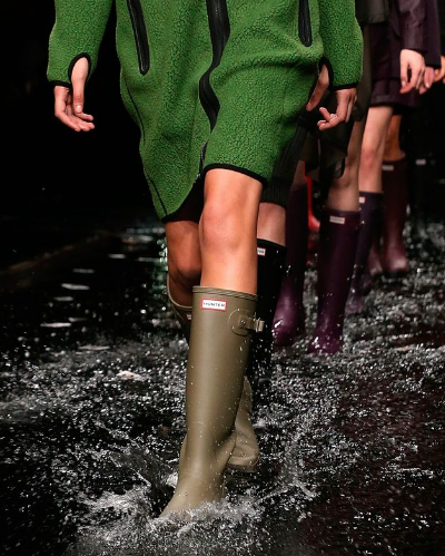 A woman walking the runway wearing a pair of green Hunter Boots