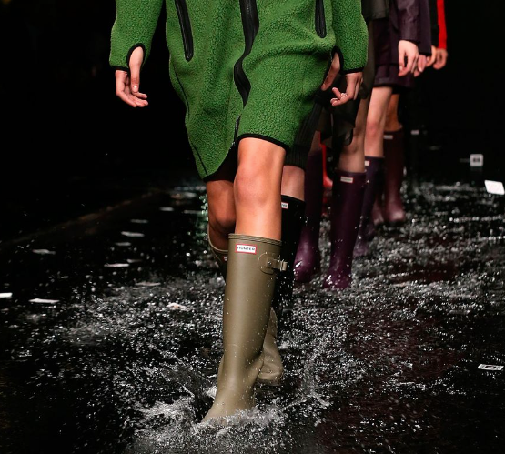 A woman walking the runway wearing a pair of green Hunter Boots